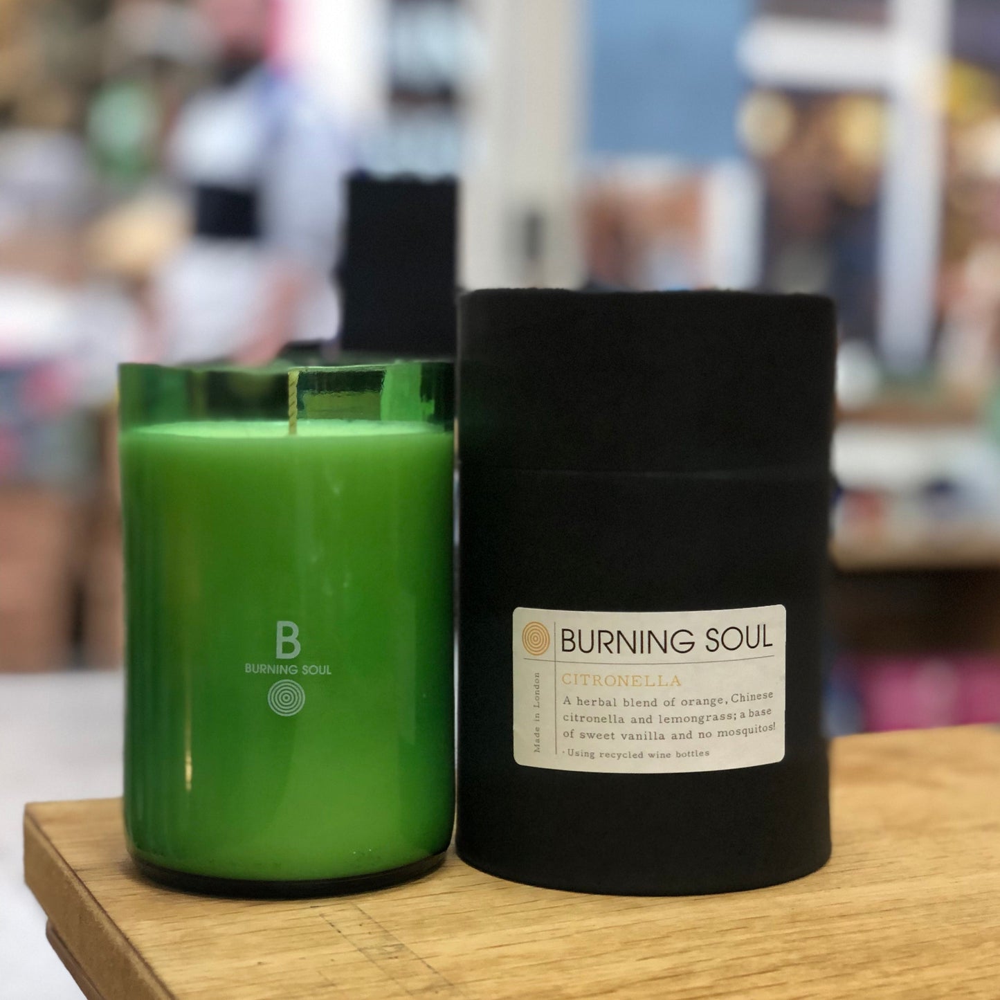green glass candle made in upcycled wine bottle by burning soul london, container is black cardboard on wooden table - burning soul london